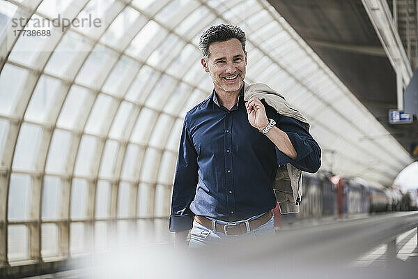 Lächelnder Mann mit Jacke läuft am Bahnhof