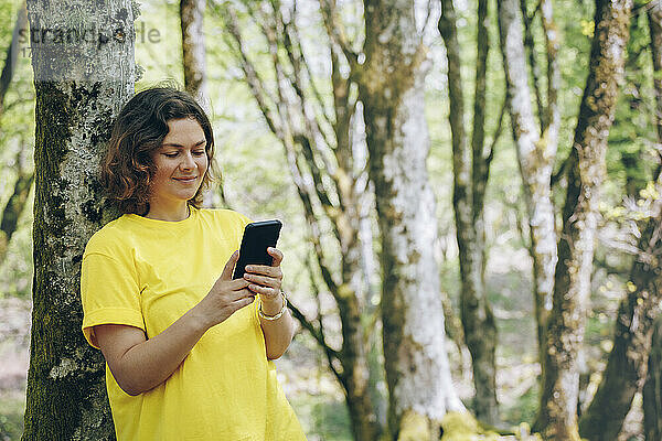 Lächelnde Frau  die im Wald Textnachrichten auf dem Mobiltelefon sendet