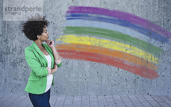 Junge Frau betrachtet die bemalte Regenbogenfahne an der Wand