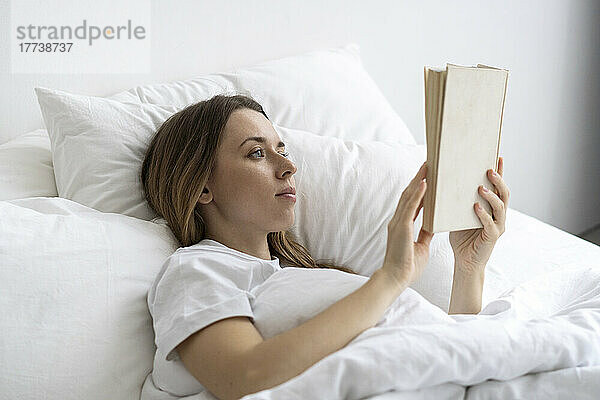 Junge Frau liest zu Hause im Bett ein Buch