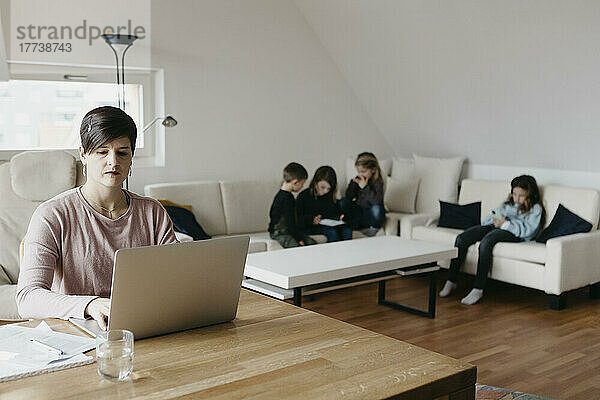 Mutter arbeitet am Laptop  Kinder sitzen zu Hause im Wohnzimmer