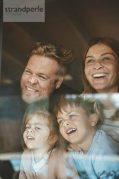 Glückliche Eltern und Kinder drücken Gesichter auf Fensterglas