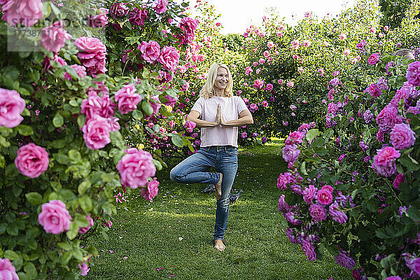 Glückliche Frau macht Baumpose-Yoga inmitten eines Rosengartens