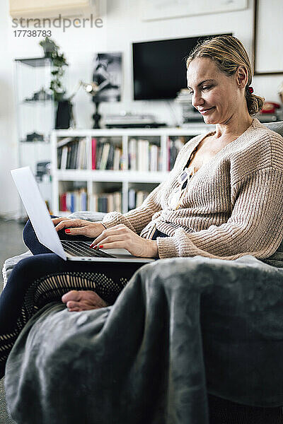 Lächelnde Frau mit Laptop  die zu Hause auf einem Sessel sitzt
