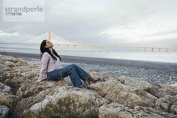 Junge Frau sitzt auf Felsen und entspannt sich am Strand am Fluss