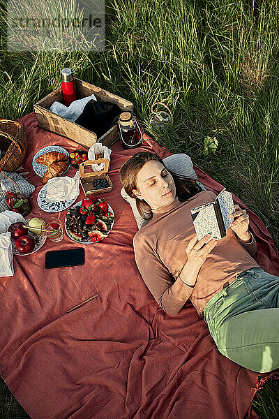 Junge Frau liest Buch auf Picknickdecke im Feld