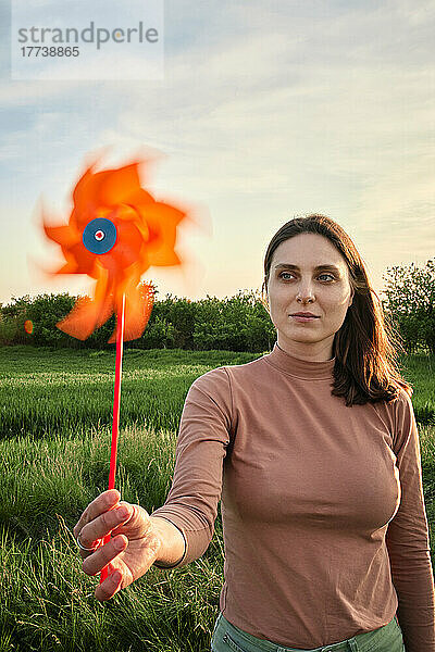 Young woman holding pinwheel toy on picnic in field at sunset