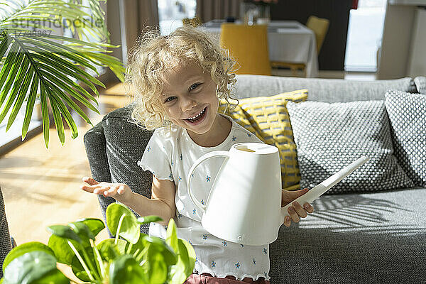 Happy girl holding watering can by sofa at home