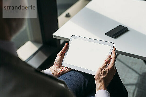 Reifer Geschäftsmann mit Tablet-PC sitzt am Schreibtisch im Büro