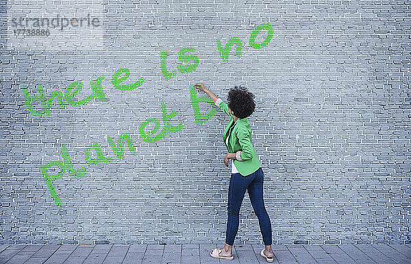 Young woman writing There is no Planet B on wall
