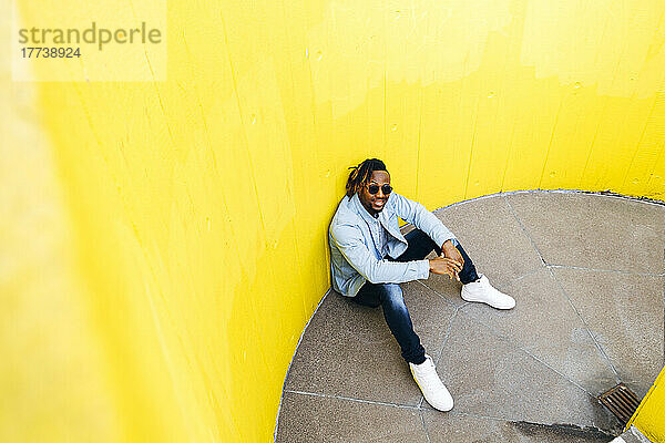 Junger Mann mit Sonnenbrille sitzt vor gelber Wand