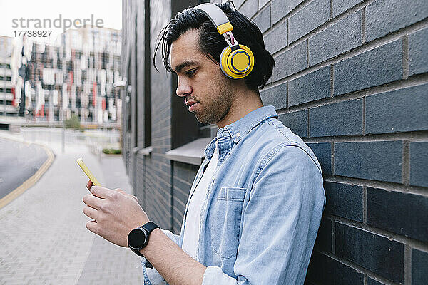 Mann mit Kopfhörern benutzt Smartphone in der Nähe der Wand