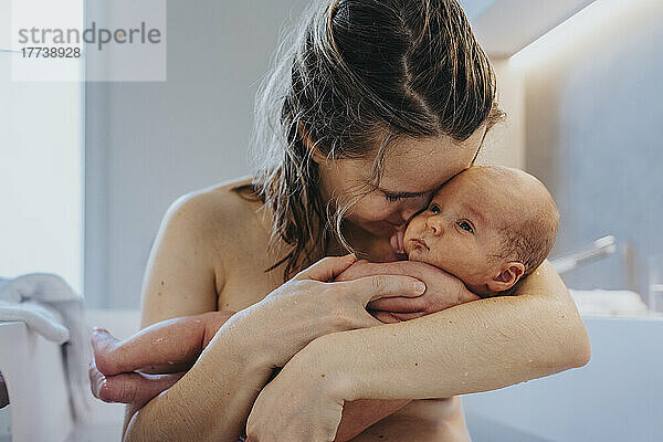 Nackte Mutter kuschelt süßes Baby zu Hause in der Badewanne