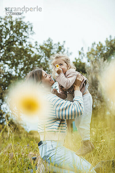 Happy young woman carrying daughter in meadow