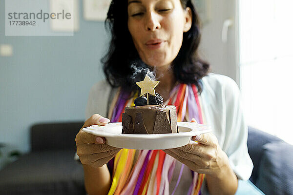 Lächelnde Frau bläst zu Hause eine sternförmige Geburtstagskerze auf dem Kuchen aus