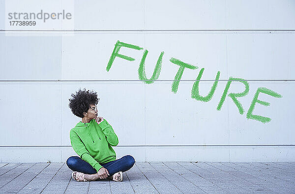Frau sitzt mit gekreuzten Beinen auf dem Boden vor dem grünen Wort „Zukunft“.