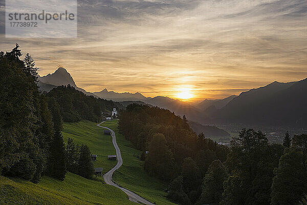 Deutschland  Bayern  Wamberg  Sonnenuntergang über einer kleinen Straße  die zu einem abgelegenen Dorf im Wettersteingebirge führt