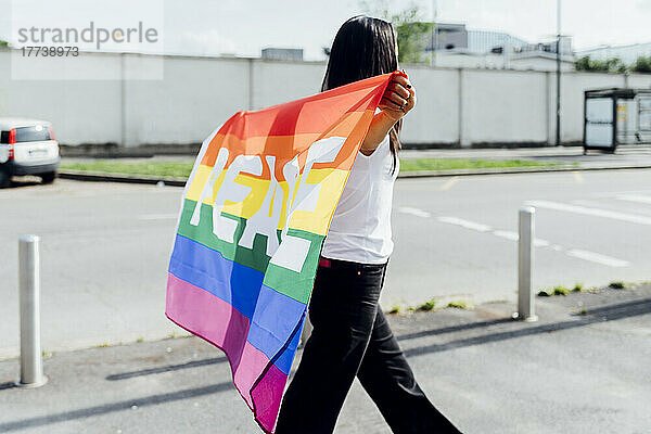 Frau mit Regenbogenfahne spaziert an sonnigem Tag