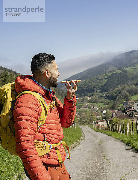 Mann mit Rucksack sendet an einem sonnigen Tag Voicemail über sein Mobiltelefon