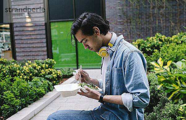 Mann isst Salat und sitzt neben Pflanzen