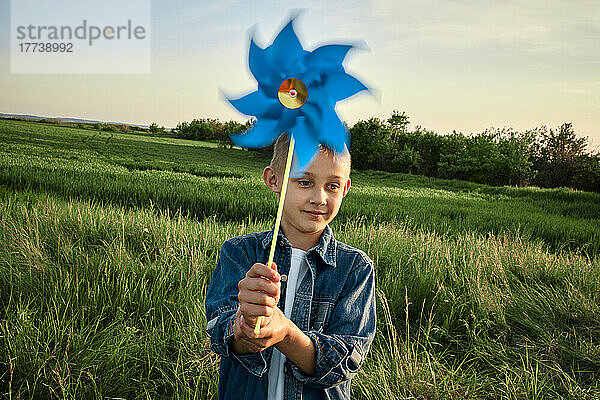 Junge hält blaues Windradspielzeug auf landwirtschaftlichem Feld