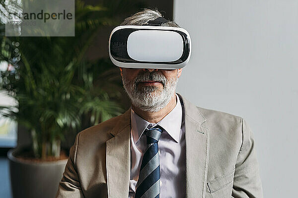 Lächelnder reifer Geschäftsmann mit Virtual-Reality-Simulator im Büro