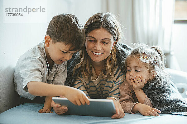 Lächelnde Mutter mit Sohn und Tochter mit Tablet-PC im Bett