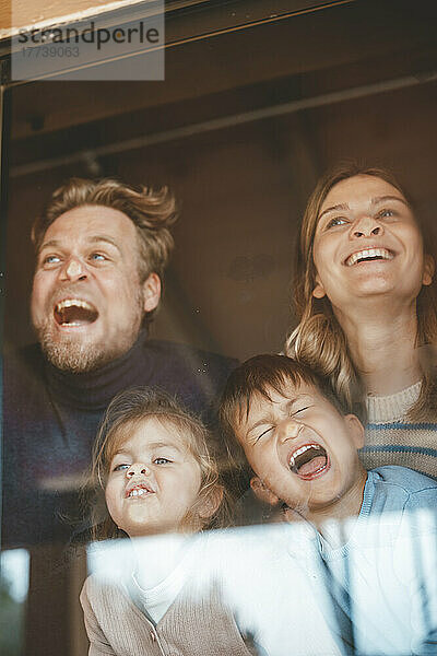 Playful parents and children pressing faces on window glass
