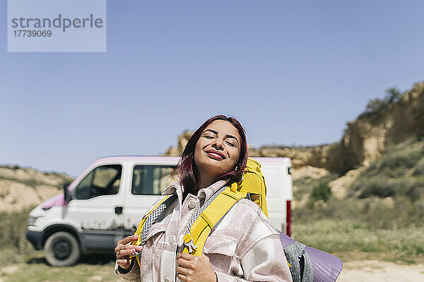 Lächelnde Frau mit Rucksack genießt sonnigen Tag