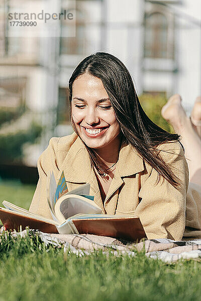 Glückliche schöne Frau  die an einem sonnigen Tag im Park liegt und ein Buch liest