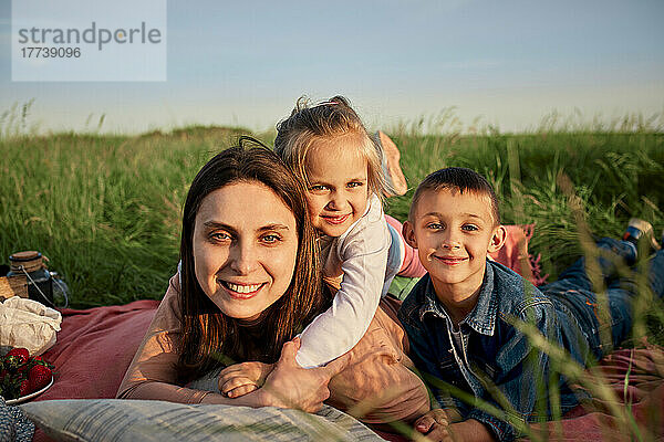 Lächelnde Mutter und Kinder liegen beim Picknick im Feld