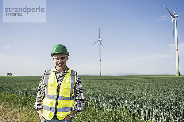 Glücklicher Ingenieur mit Schutzhelm  der vor Windkraftanlagen steht