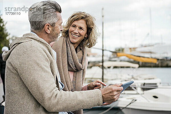Lächelnde Frau im Gespräch mit Mann  der einen Tablet-PC im Hafen hält