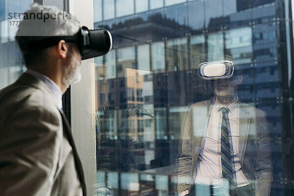 Reifer Geschäftsmann mit Virtual-Reality-Simulator steht vor dem Fenster