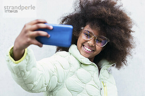 Smiling girl taking selfie through smart phone