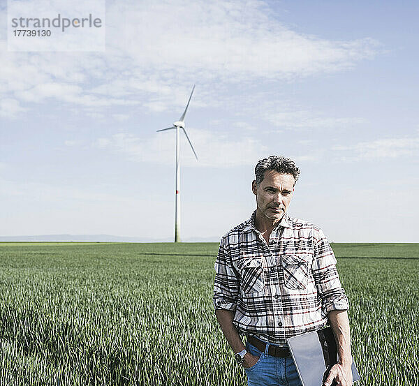 Ingenieur mit Tablet-PC steht vor Windkraftanlage