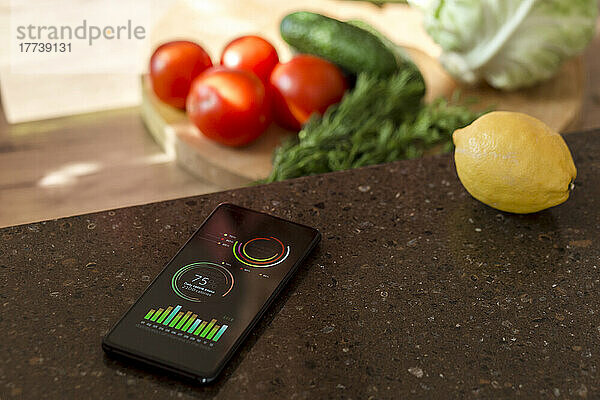 Smartphone mit Diagrammen auf der Küchentheke neben Gemüse