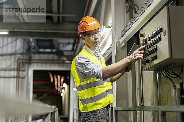 Arbeiter mit Tablet-PC drückt die Drucktaste des Bedienfelds in der Industrie