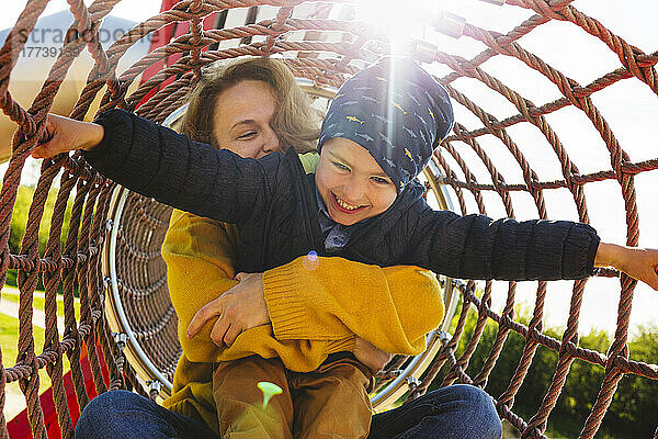 Glücklicher Junge mit Mutter  die im Klettergerüst auf dem Spielplatz spielt