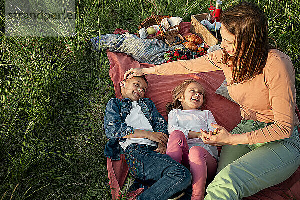 Mutter sitzt neben glücklichen Kindern auf einer Picknickdecke