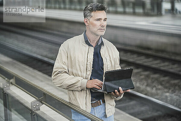 Geschäftsmann mit Tablet-PC steht am Bahnhof