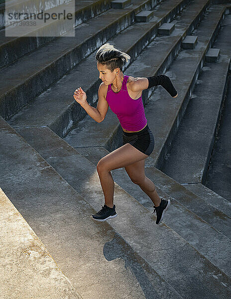 Sportliche Frau mit amputierter Hand rennt Stufen hinauf