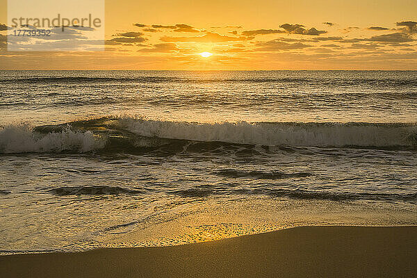 Ruhige Meereswelle bricht bei Sonnenaufgang auf den Sandstrand