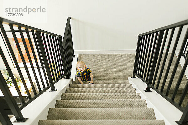Kleiner Junge (12–17 Monate) am Fuß der Treppe zu Hause