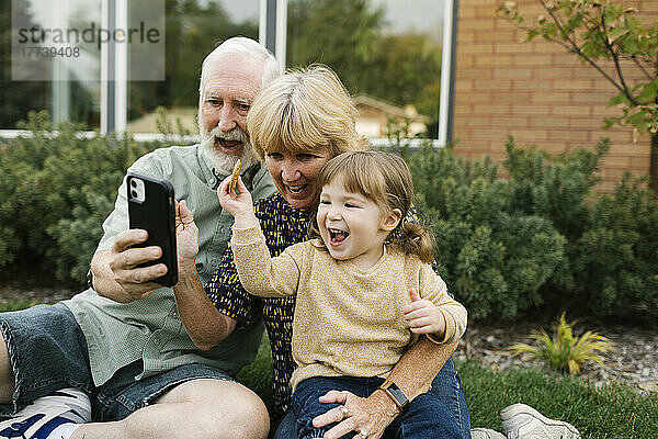 Lächelnde Großeltern machen ein Selfie mit ihrer Enkelin (4–5) im Hinterhof