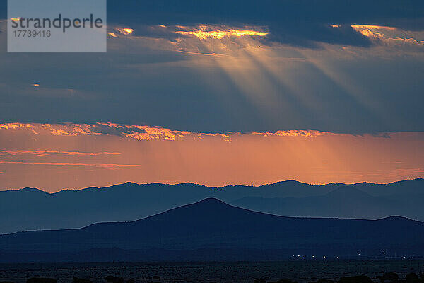 USA  New Mexico  Santa Fe  Sonnenstrahlen scheinen bei Sonnenuntergang durch Gewitterwolken über Bergen