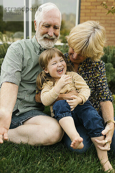 Lächelnde Großeltern mit Enkelin (4-5) im Hinterhof