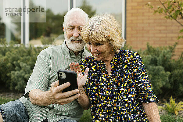 Lächelndes älteres Paar  das im Hinterhof einen Videoanruf führt