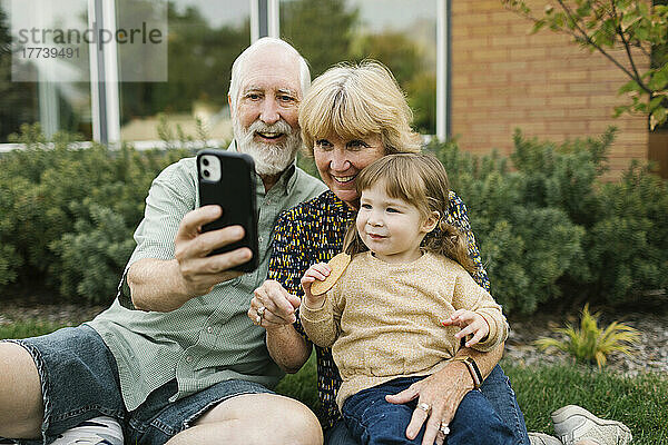 Lächelnde Großeltern machen ein Selfie mit ihrer Enkelin (4-5) im Hinterhof