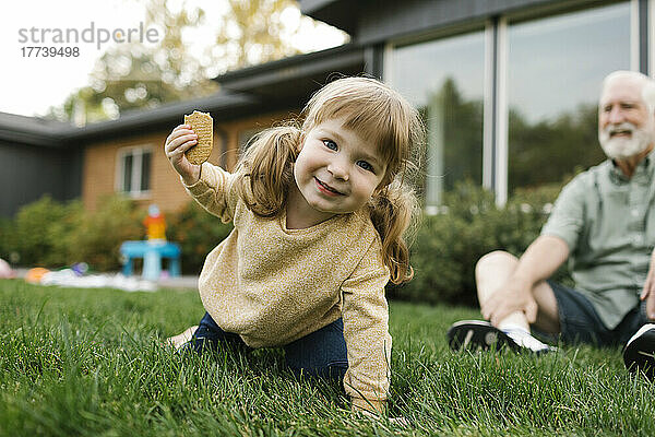 Lächelndes Mädchen (4-5) auf dem Rasen  Großvater im Hintergrund